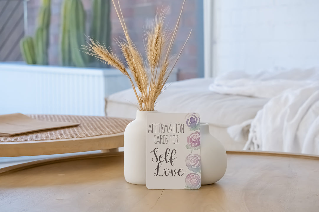 Image of a deck of affirmation cards, seen from the front and propped up by a white vase. This image is perfect for those searching for affirmation cards, positivity, self-care, and personal growth
